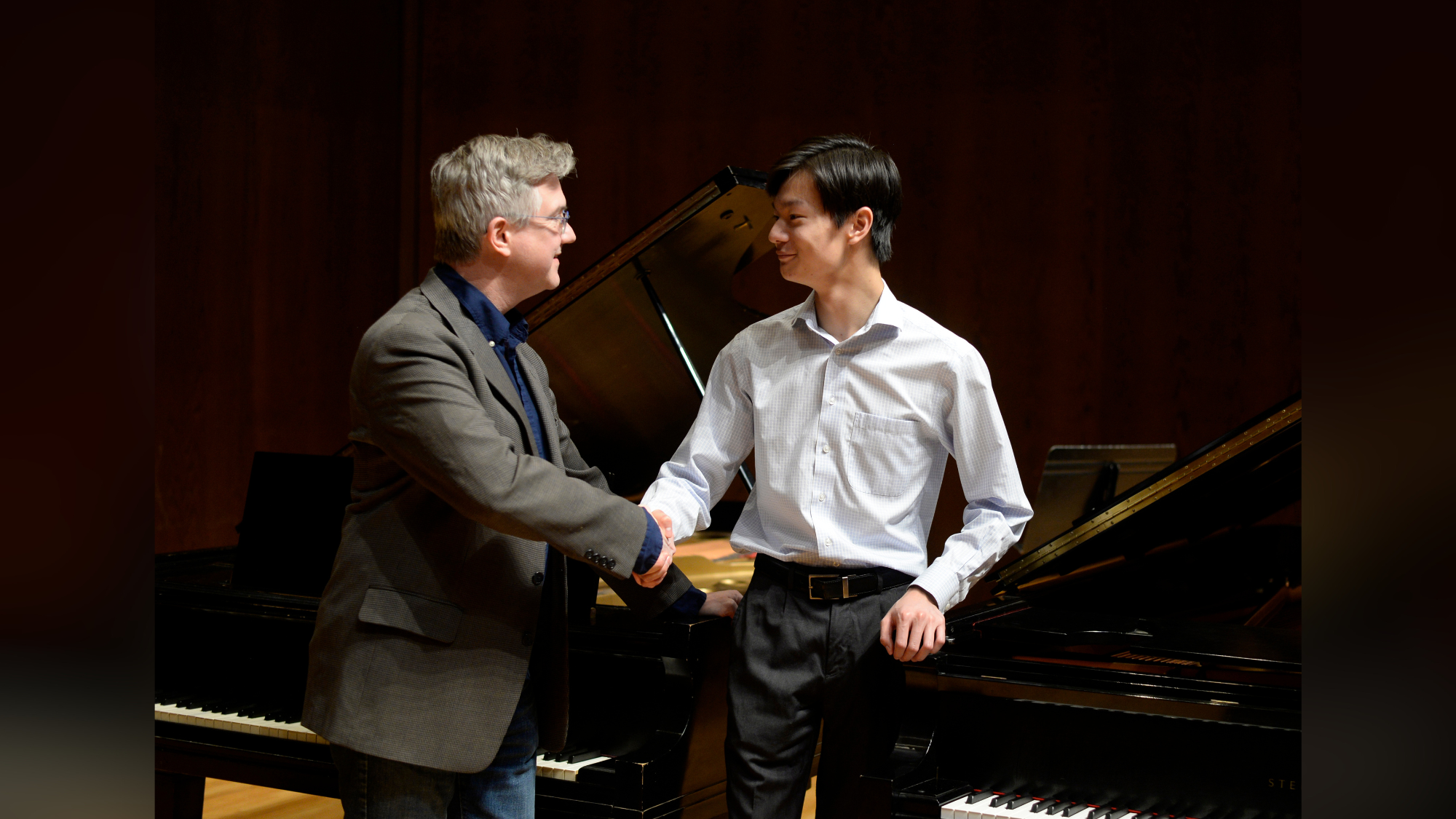 man and teenage boy shaking hands in front of piano